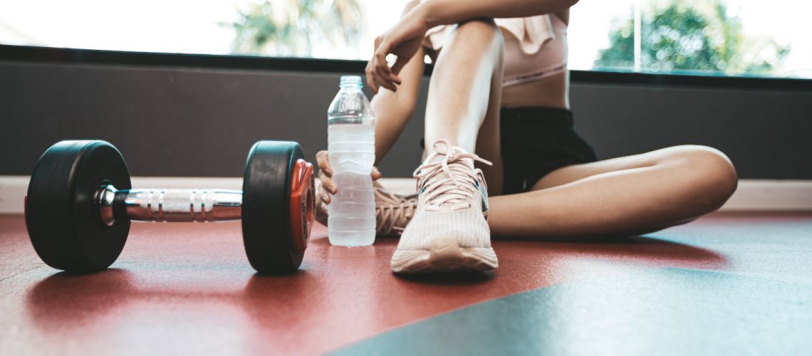 Women sit back and relax after exercise. There is a water bottle and dumbbells,selective focus